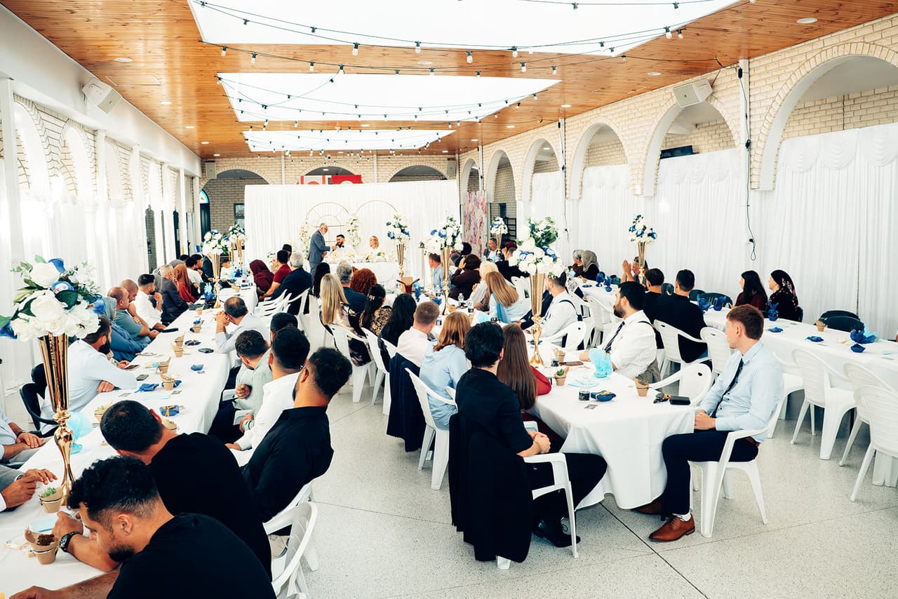 The reception hall at the Sunshine Mosque, full of family and friends at long white tables