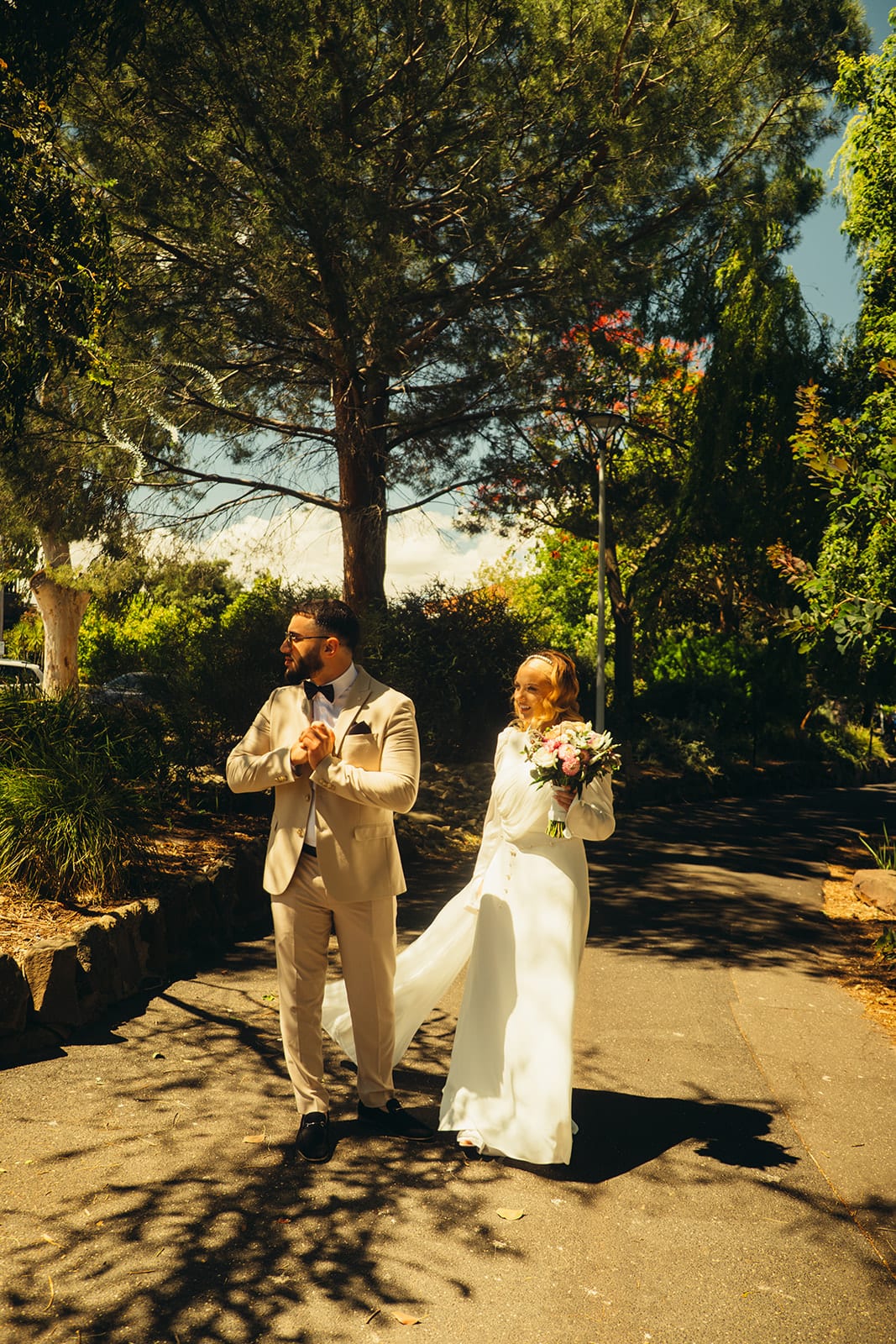 Elektra and Yasir walking along a shaded garden path under tall pines, her veil lifting behind her