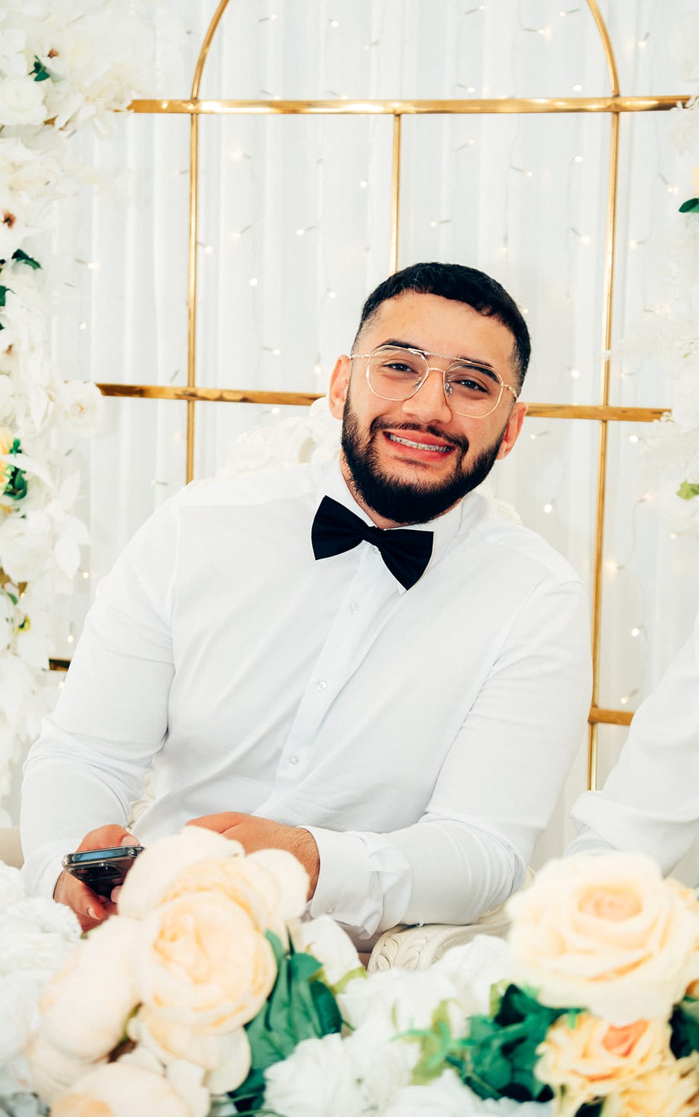 Yasir grinning at the head table behind white and peach roses