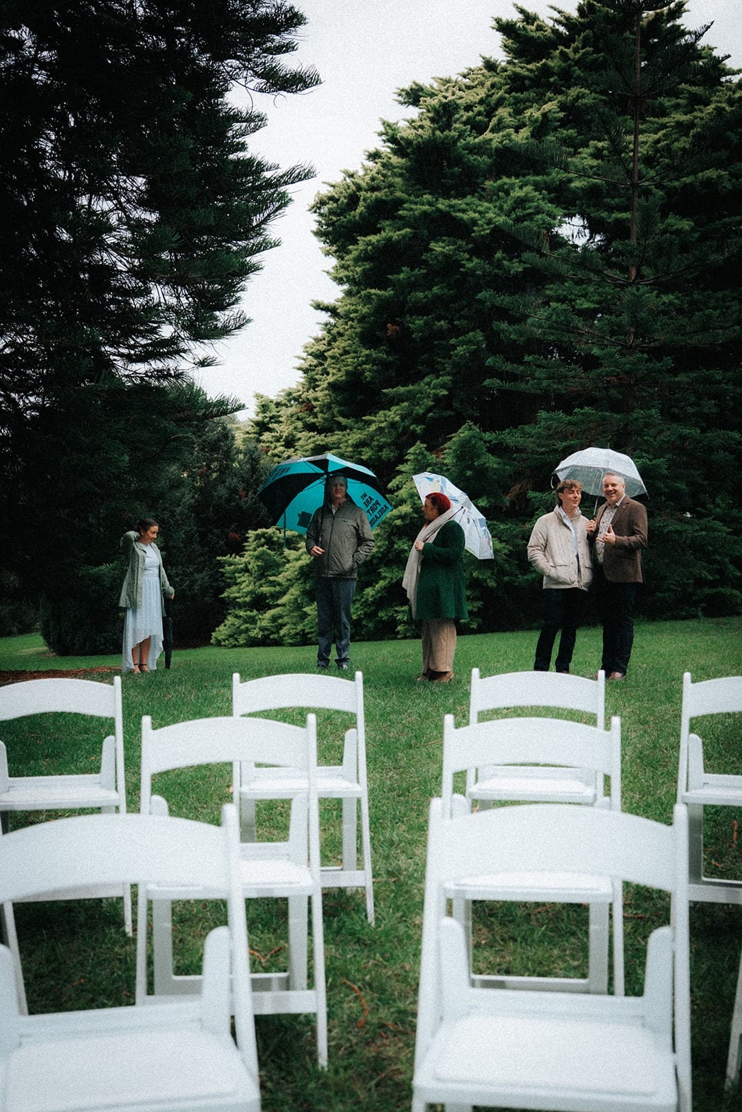 Guests arriving with umbrellas behind rows of white folding chairs