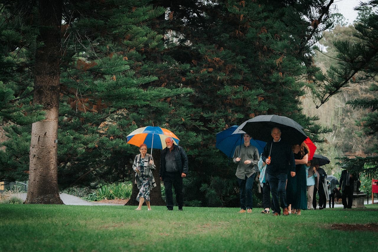 Guests with orange and black umbrellas crossing the lawn beneath the pines