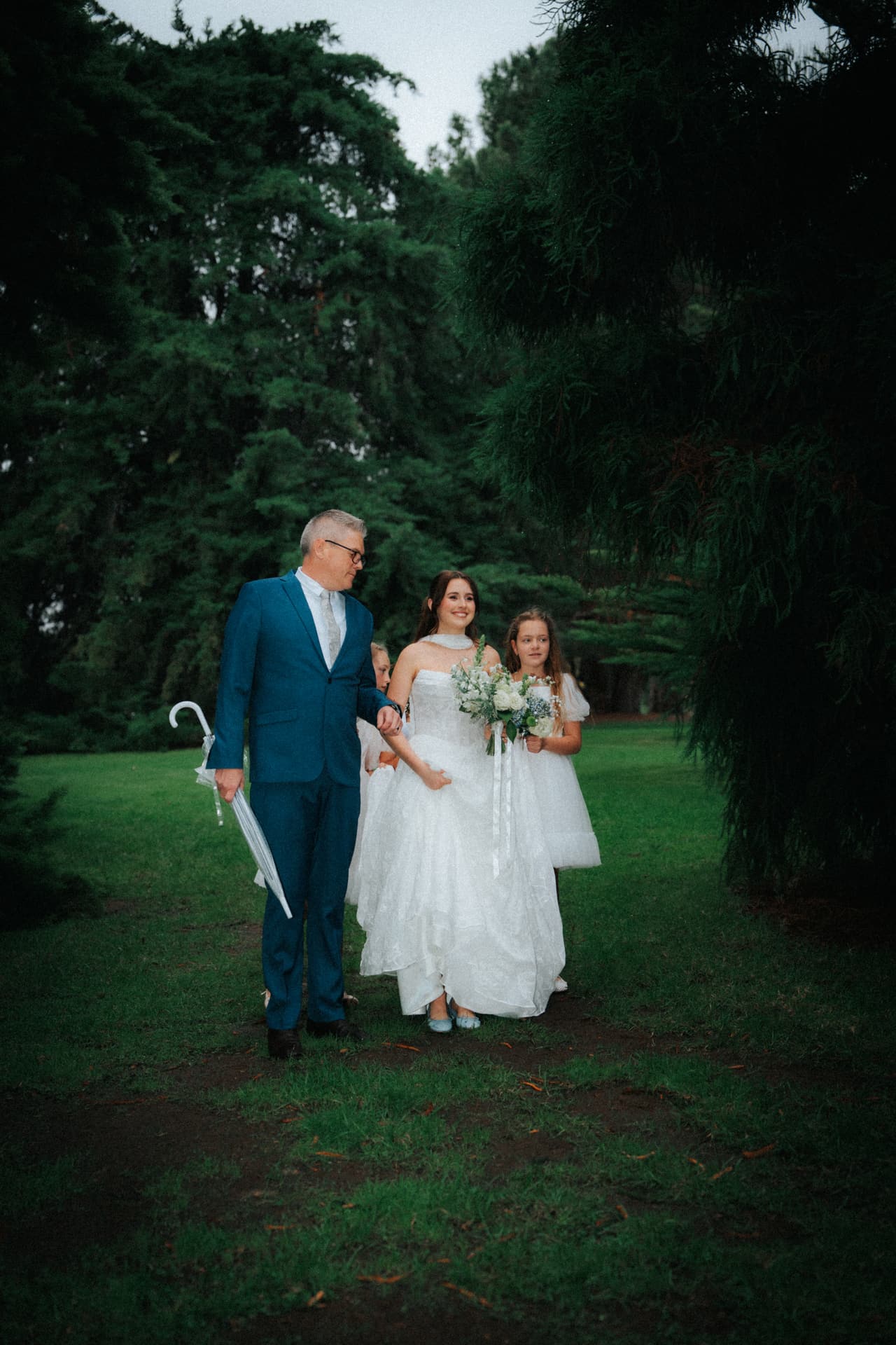 Charlotte walking down the aisle with her father, who carries a folded umbrella