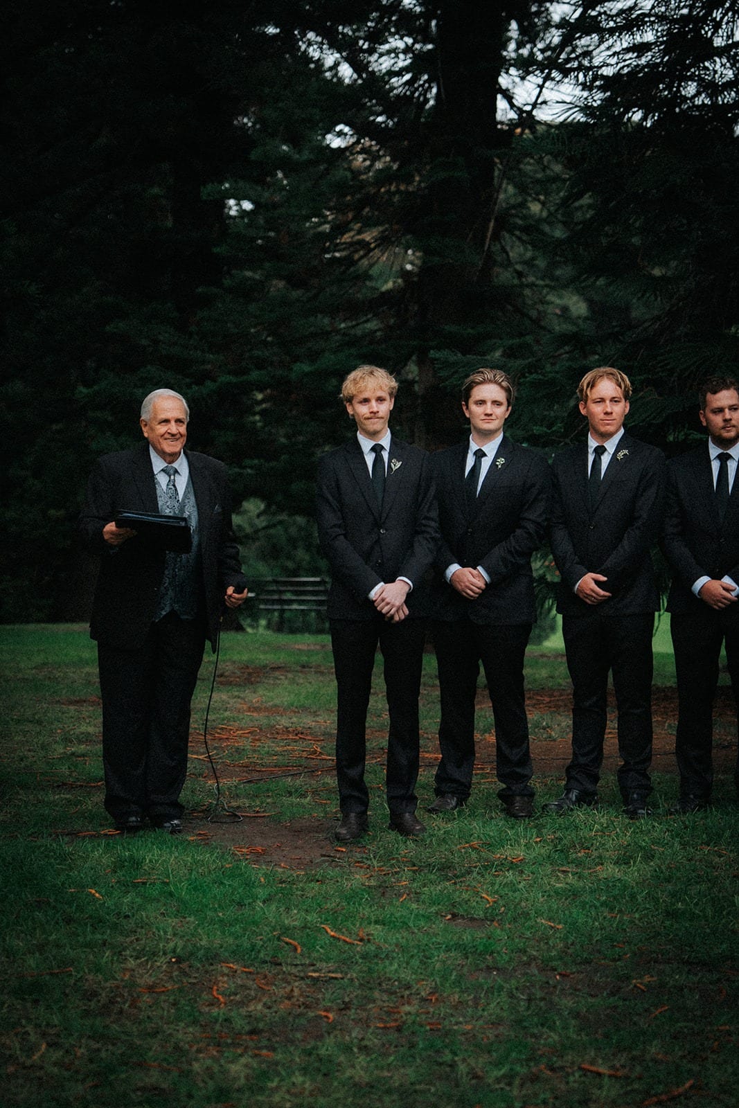 The celebrant and groomsmen waiting at the front of the ceremony under the trees
