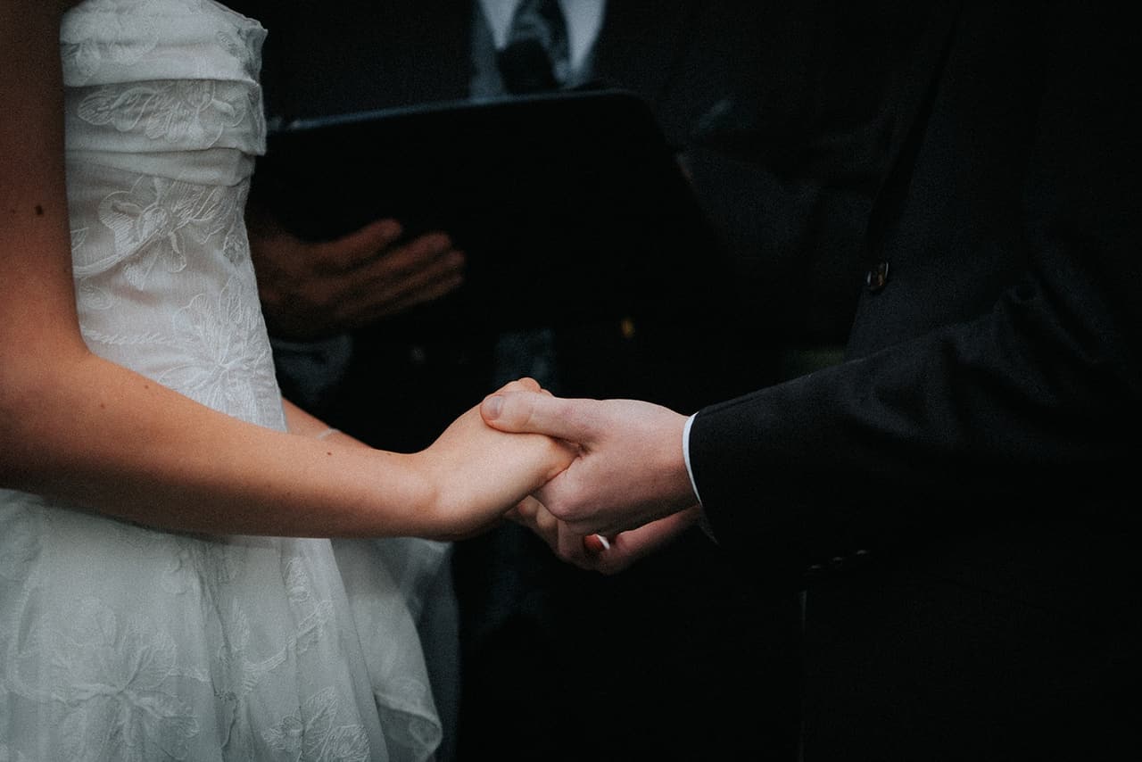 Close-up of Eli and Charlotte holding hands as the celebrant reads