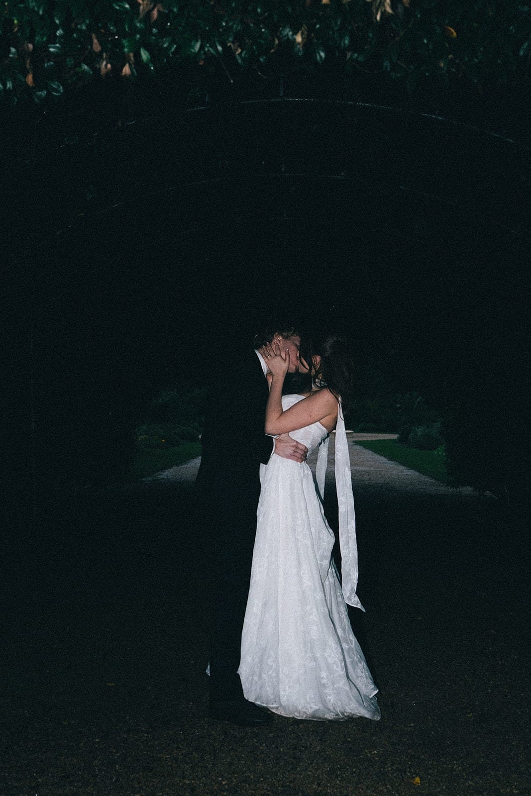 Eli and Charlotte kissing on a dark garden path as the light fades