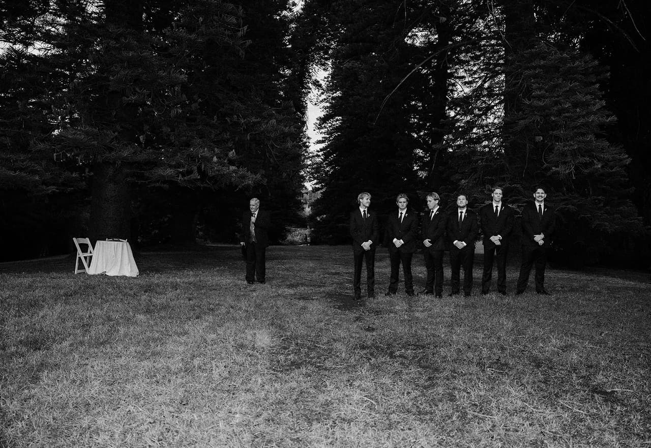 Black and white wide photo of the groomsmen at the edge of the pine avenue
