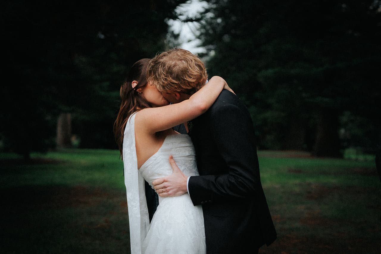 Eli and Charlotte kissing in a close embrace under the pines, her arms around his neck
