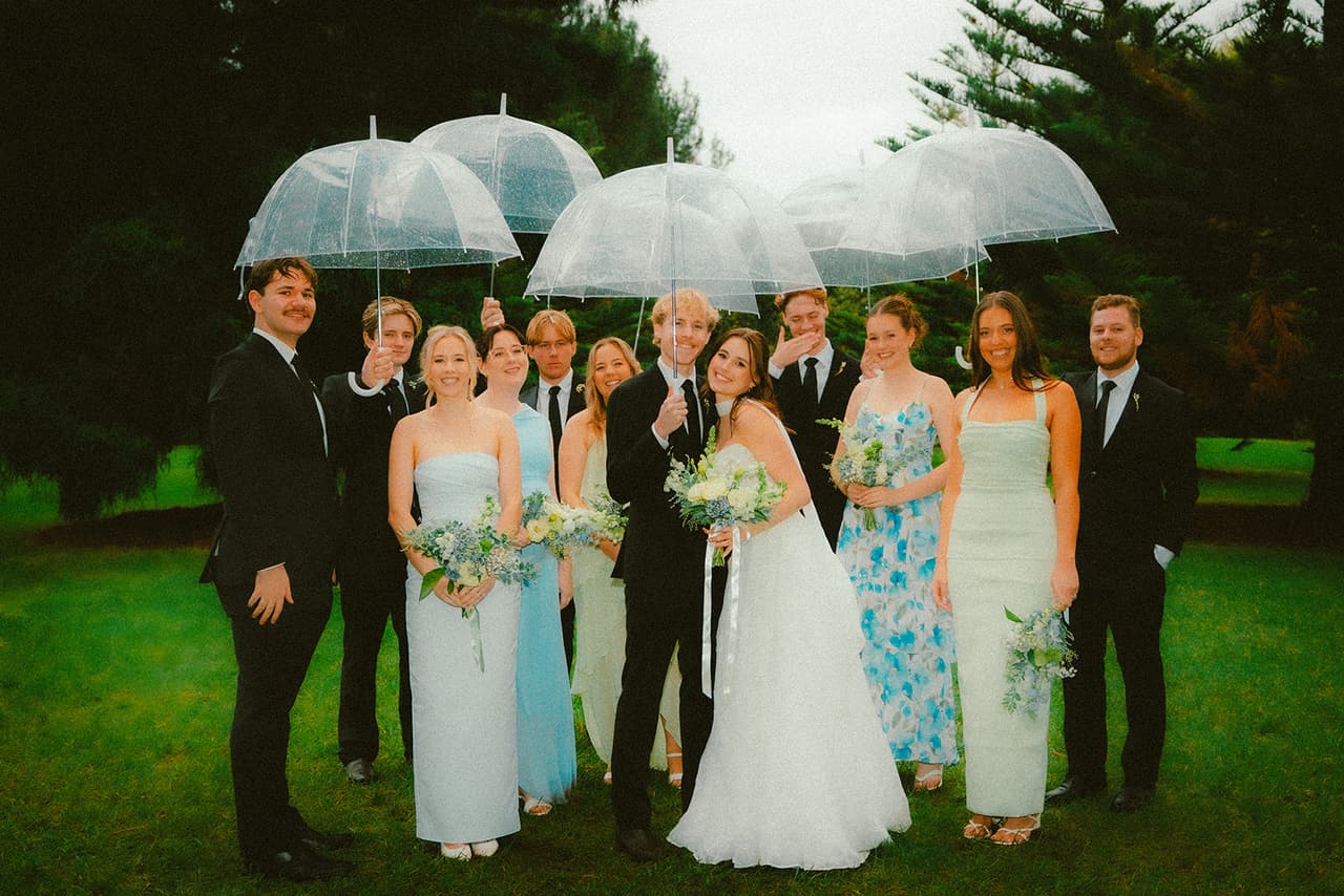 Eli, Charlotte and their bridal party under a canopy of clear umbrellas on the lawn