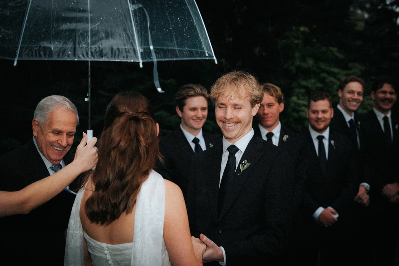 Eli laughing as he holds Charlotte’s hands, the celebrant and the groomsmen grinning around them