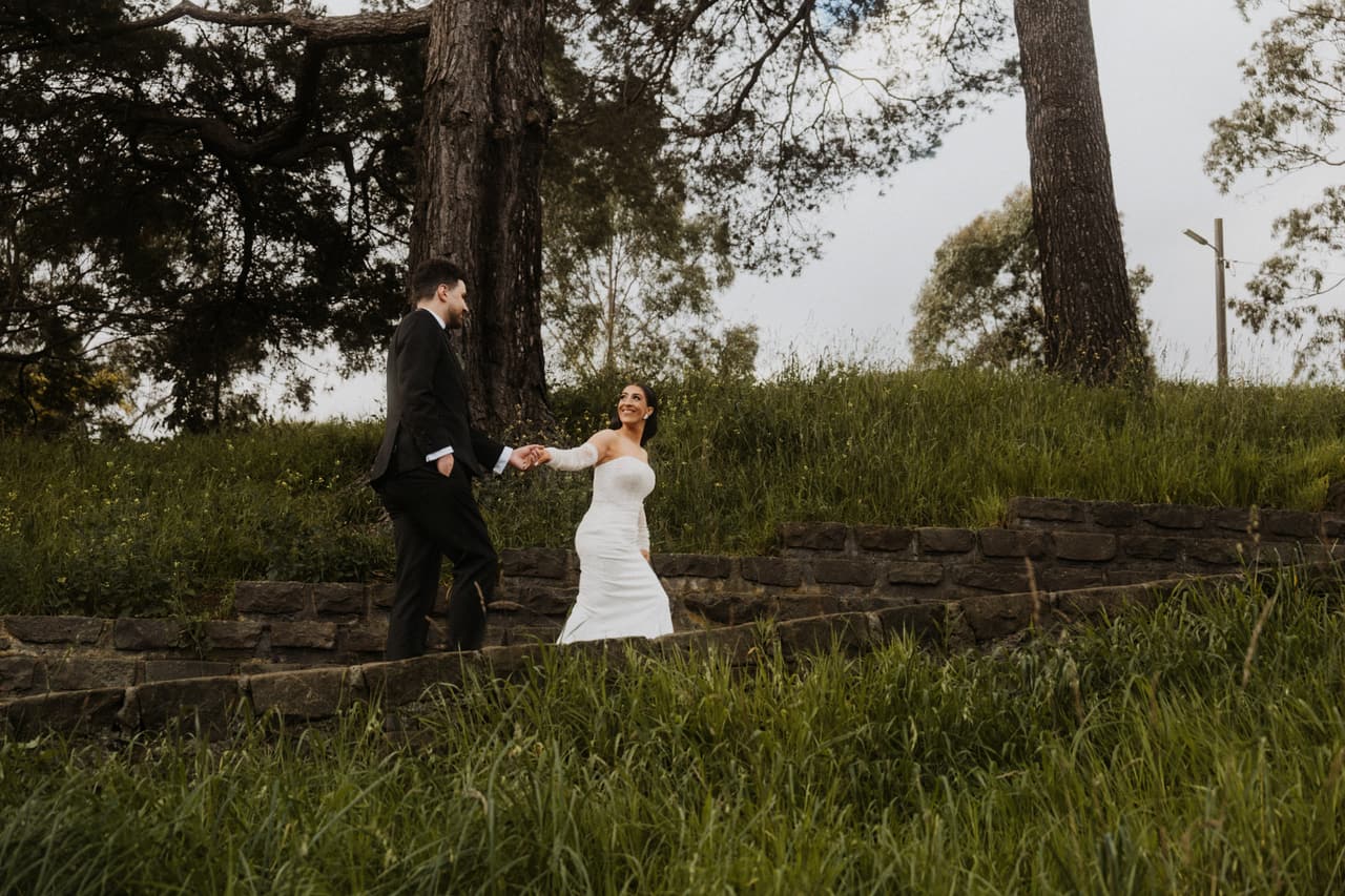 George and Tia holding hands as they walk across the grassy terraces under tall gums