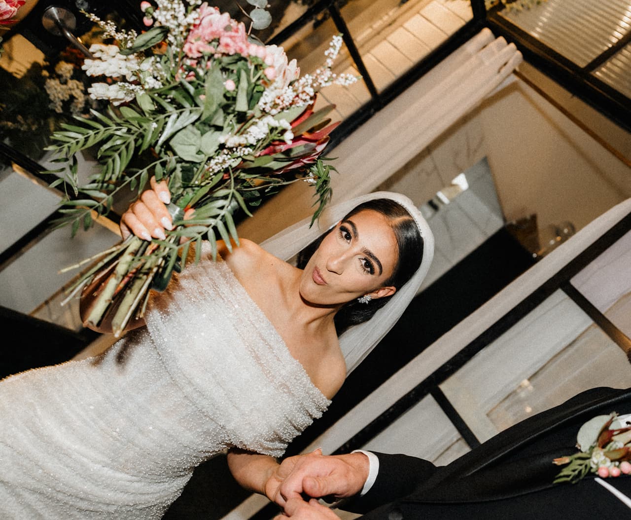 Tia raising her bouquet and laughing as she walks out of the ceremony, the frame tilted