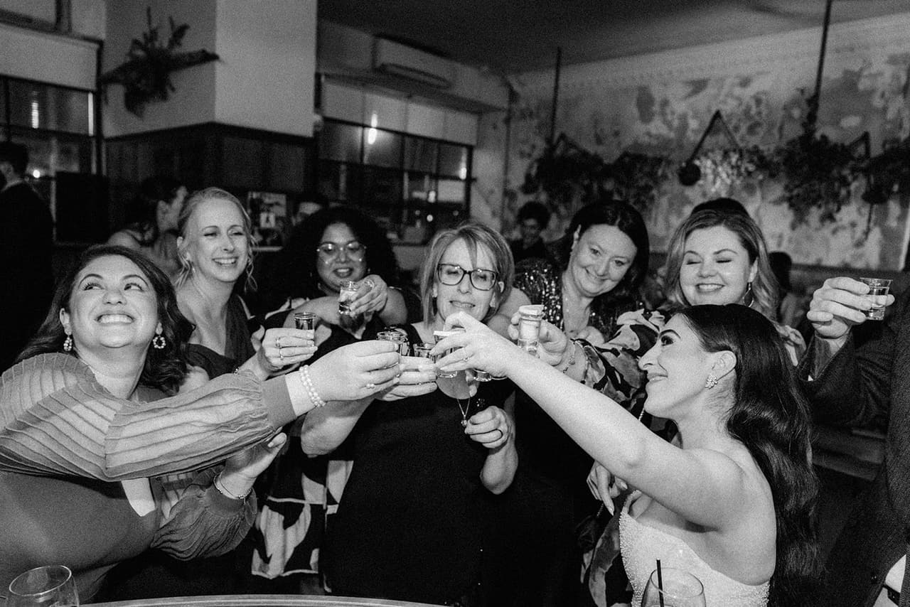Black and white photo of Tia and her friends clinking shot glasses at the bar