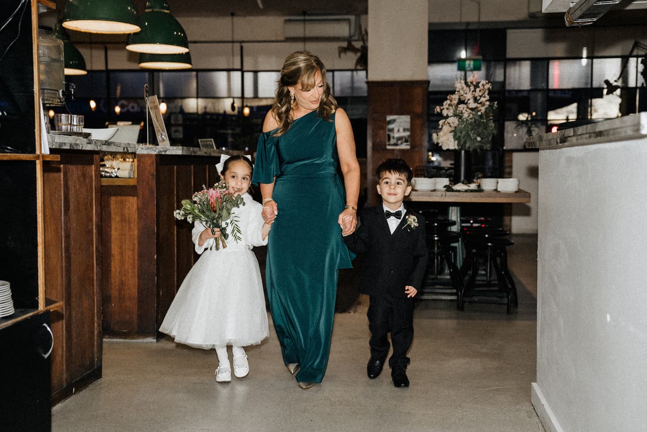 The flower girl and page boy walking in through the restaurant with a woman in a green dress