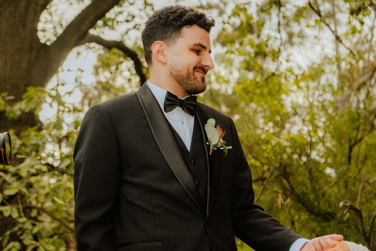 George laughing in his tuxedo among green trees, one hand held out
