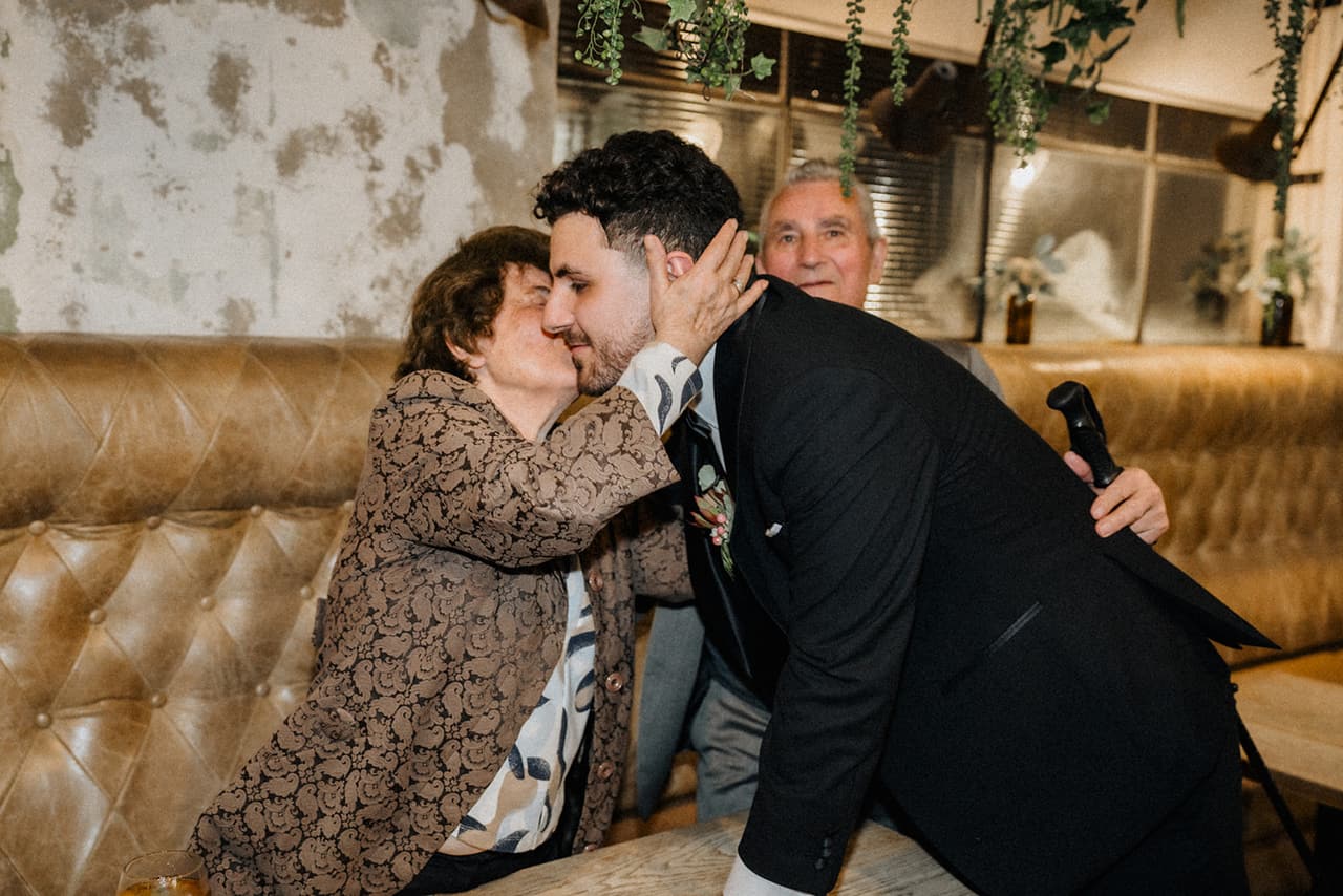 An older woman kissing George on the cheek on the leather banquette