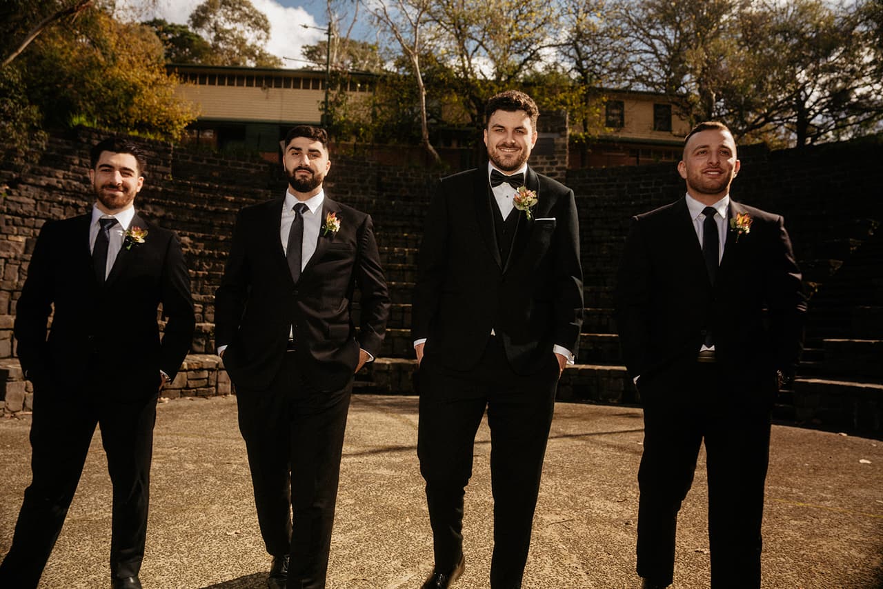 George and his groomsmen in black suits standing in a row in the amphitheatre