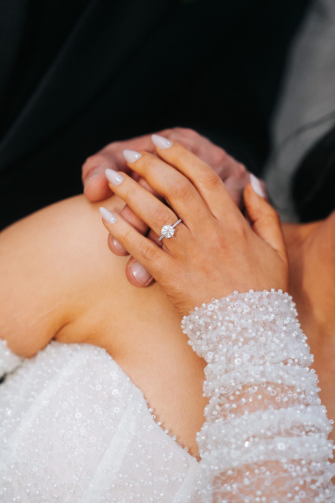 Close up of Tia’s hand with her ring resting on George’s shoulder, her sleeve covered in beads