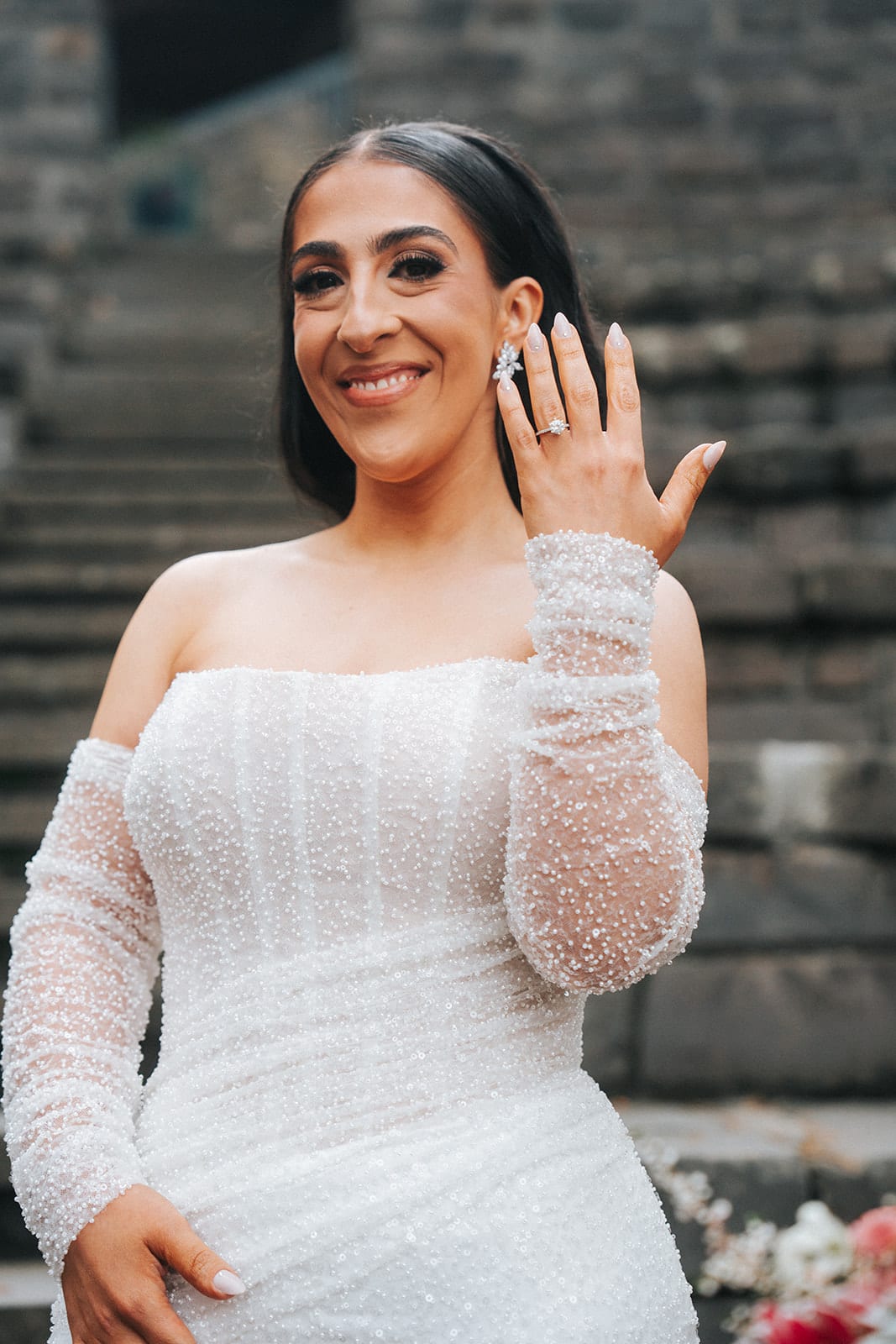 Tia laughing as she holds up her engagement ring, in a long-sleeved beaded gown
