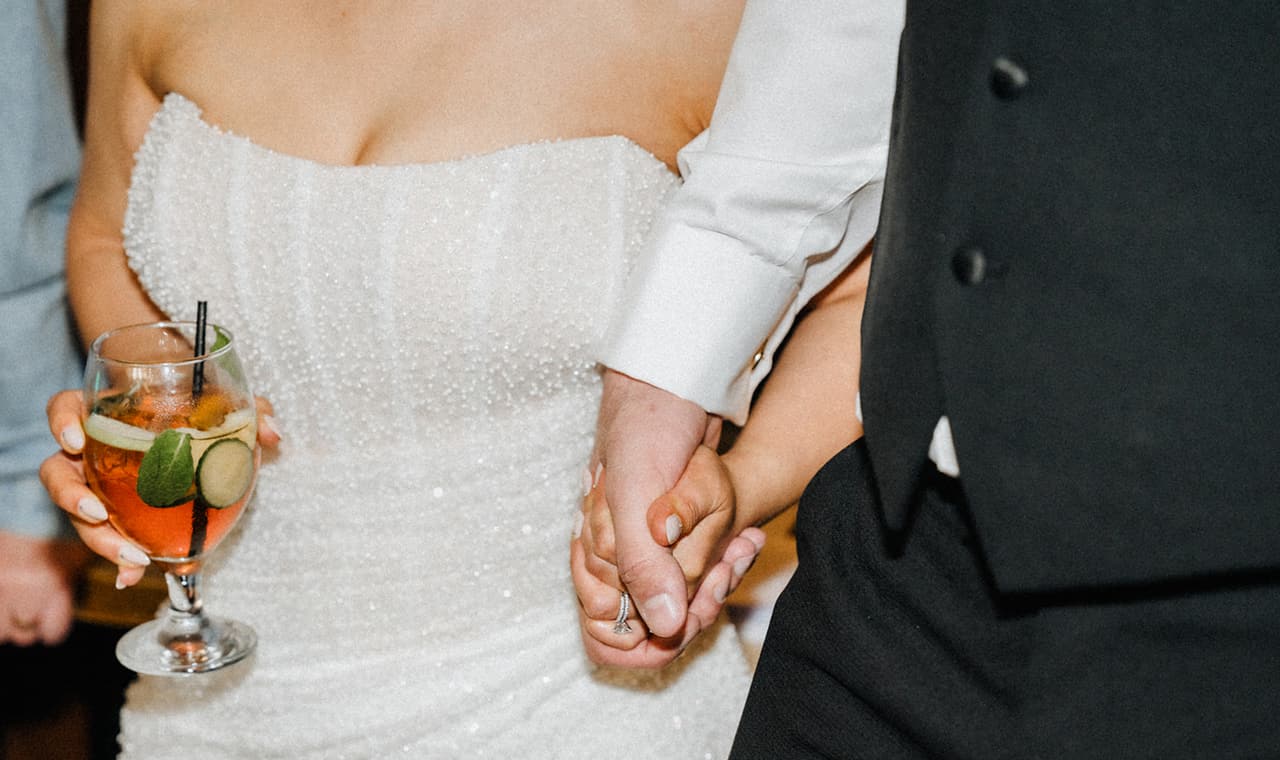 Close up of Tia holding a spritz in one hand and George’s hand in the other