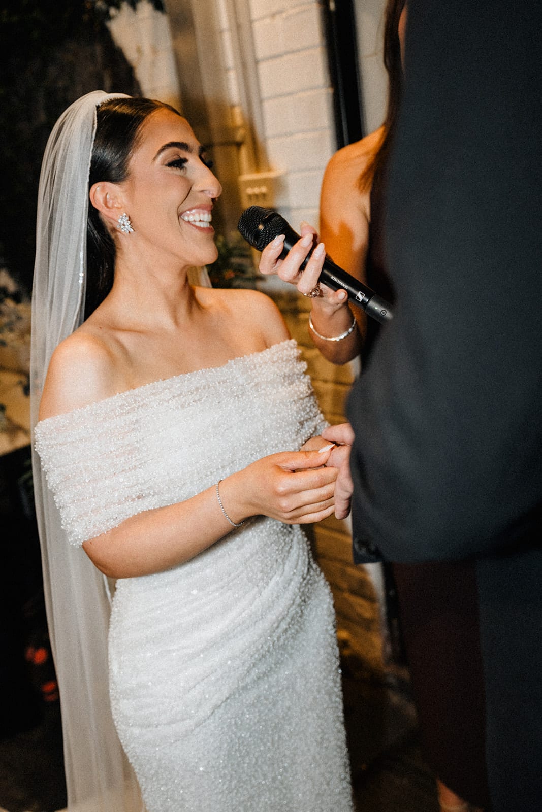 Tia reading her vows into a microphone, her veil falling down her back