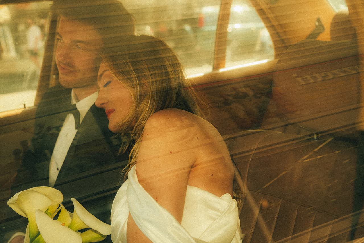 Hannah leaning towards Josh with her eyes closed in the back seat, seen through reflections in the car window