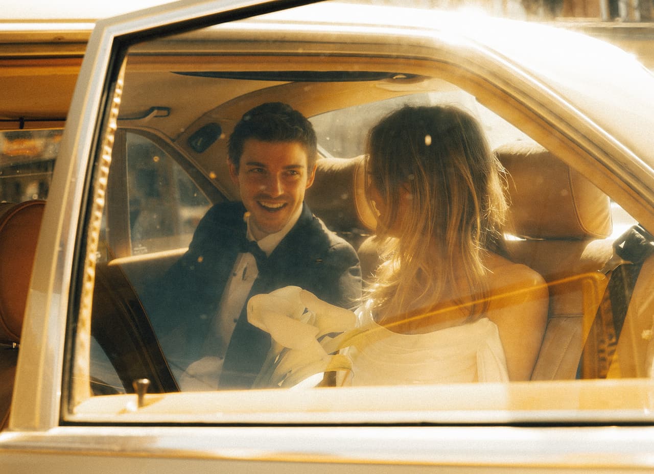 Hannah and Josh laughing in the back seat of the Mercedes, seen through its window