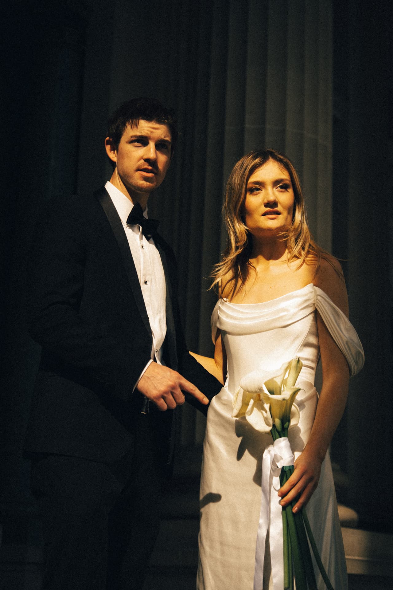 Hannah and Josh side by side in deep shade, Hannah holding white calla lilies