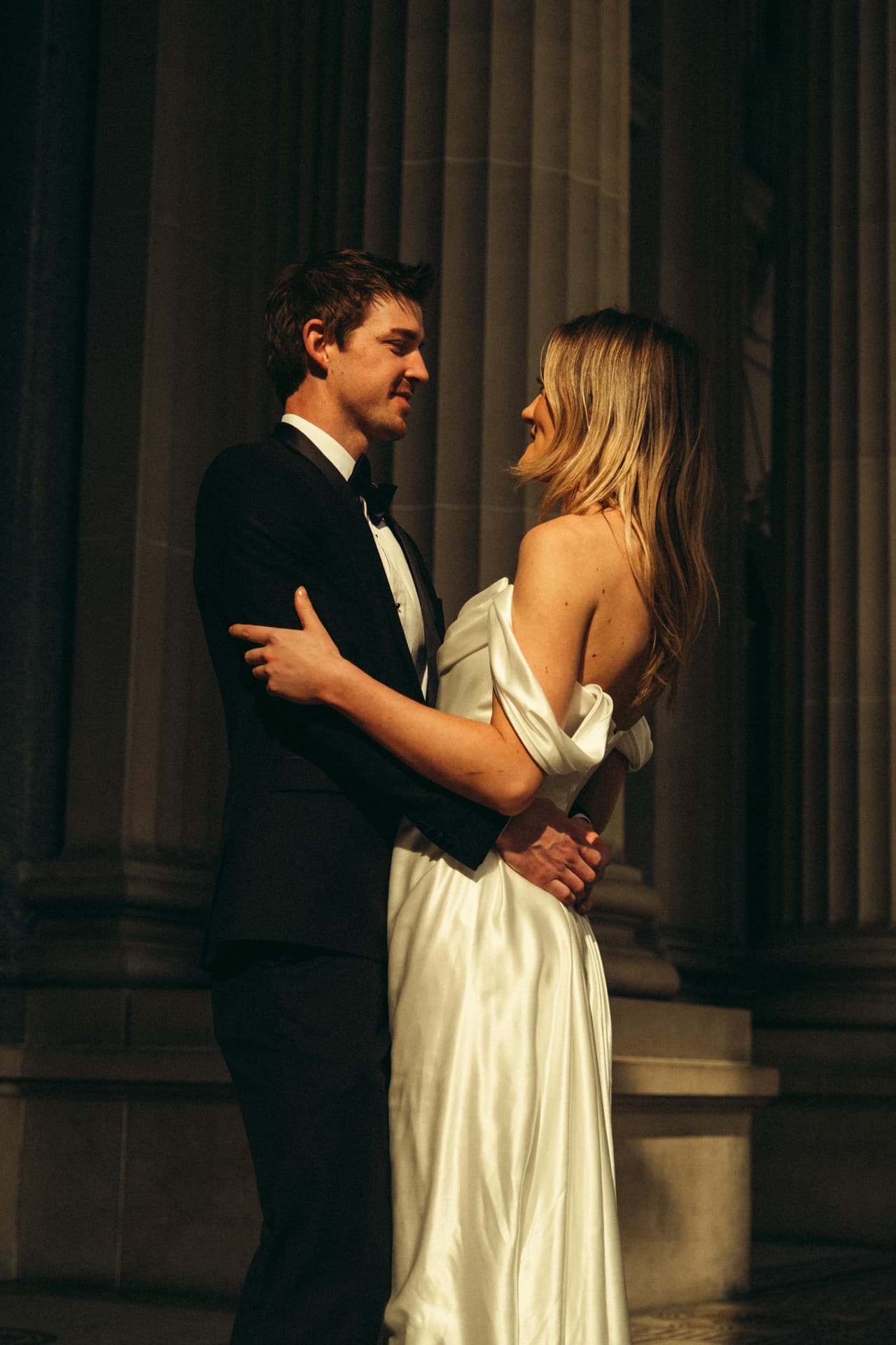 Josh holding Hannah close between the stone columns in the evening shade