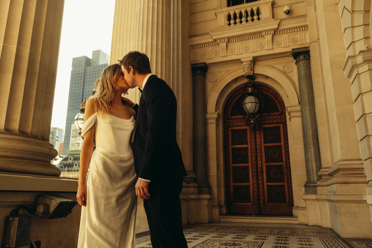 Hannah and Josh kissing beside the arched doorway of Parliament House