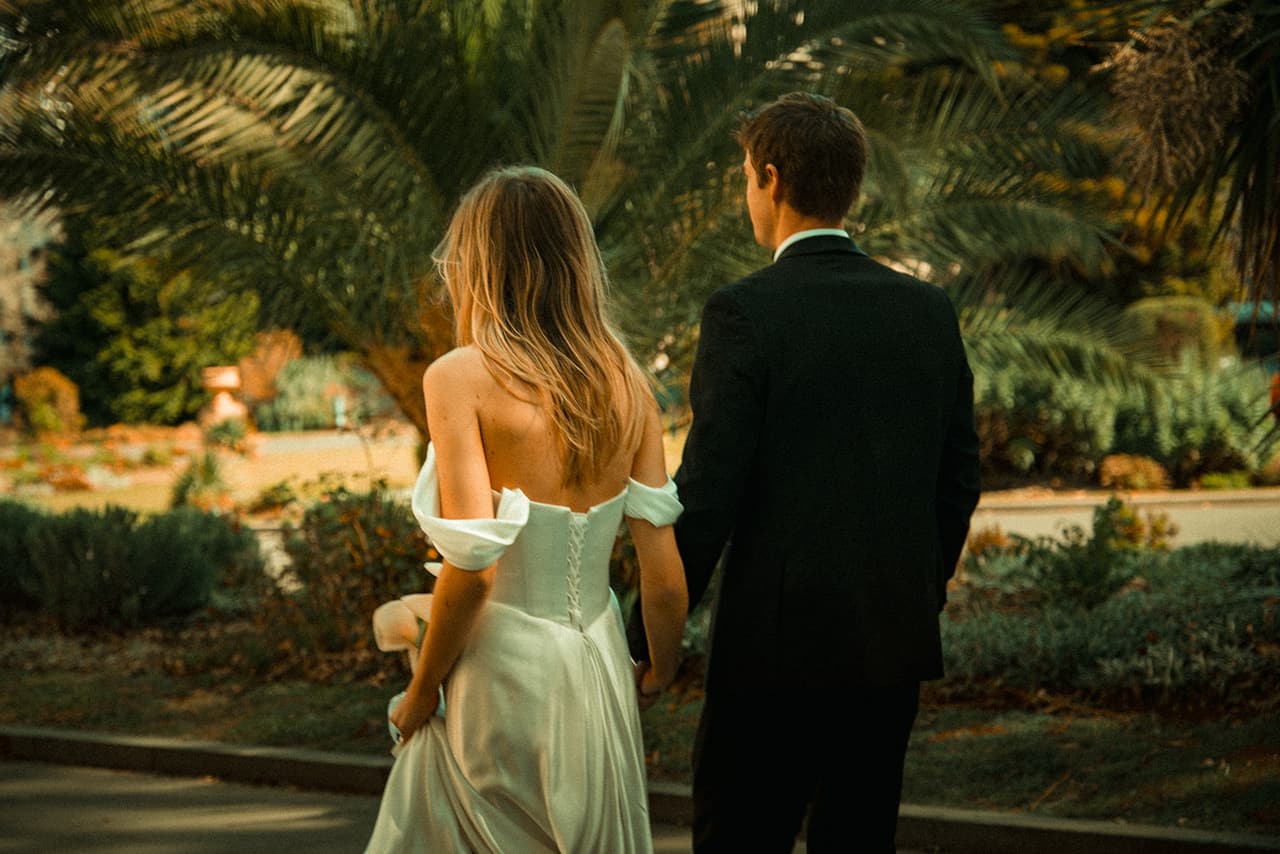 Hannah and Josh seen from behind among the palms and flower beds of Carlton Gardens