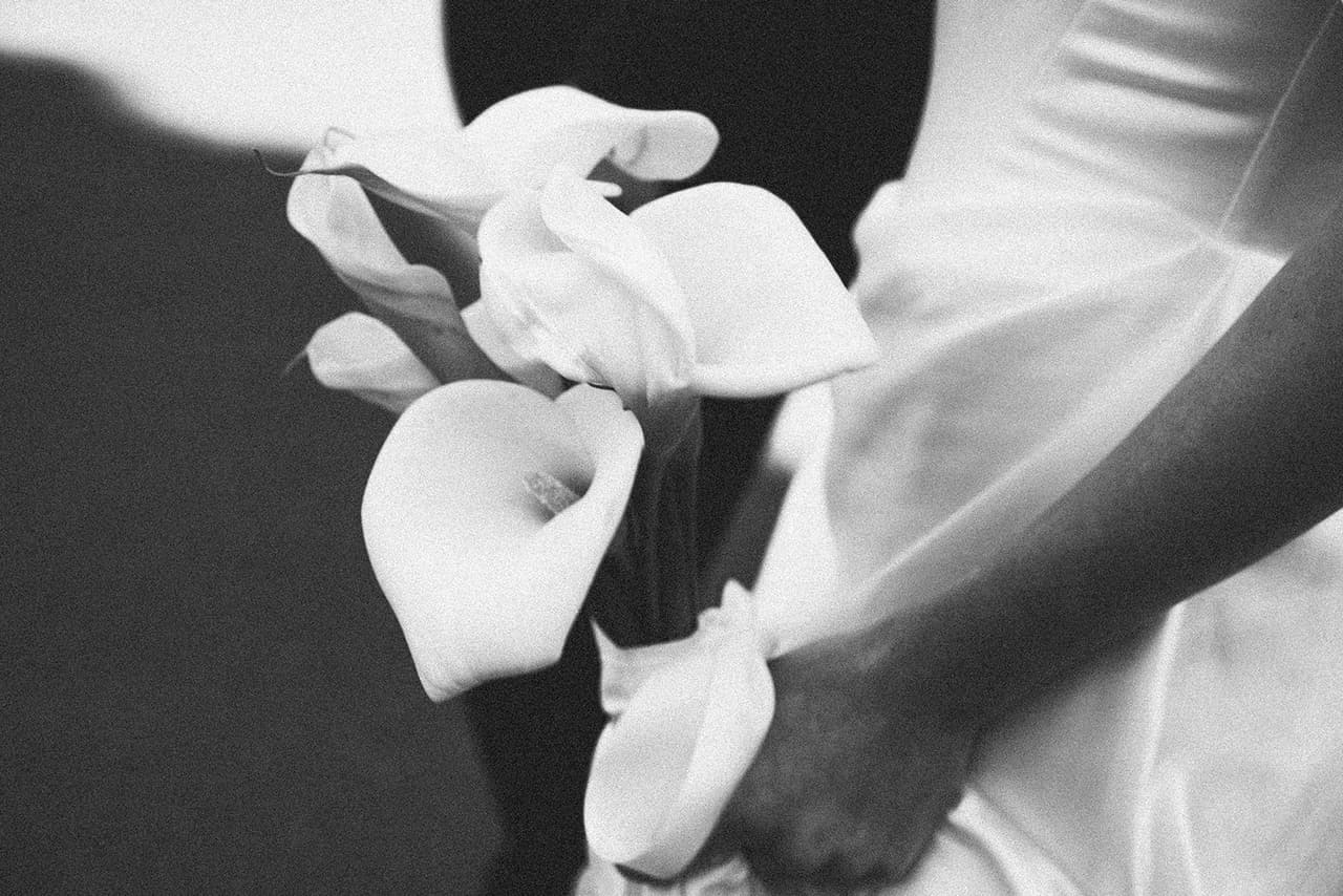 Black and white close up of white calla lilies against Hannah’s satin gown