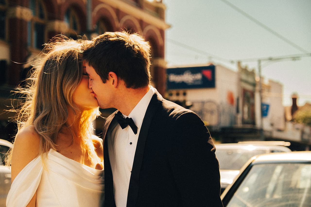 Hannah and Josh kissing in the sun on the street, the old Mercedes beside them