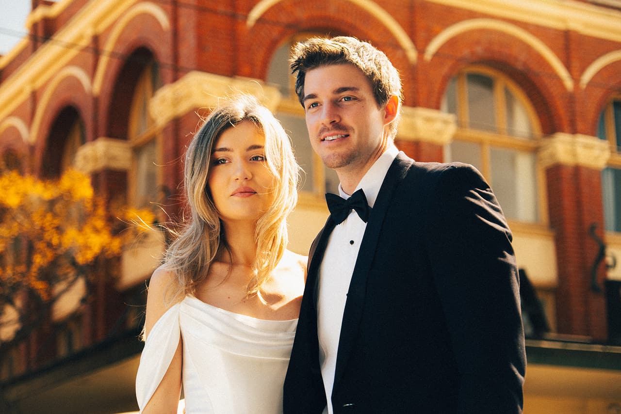 Hannah and Josh side by side in the sun in front of the red brick arches