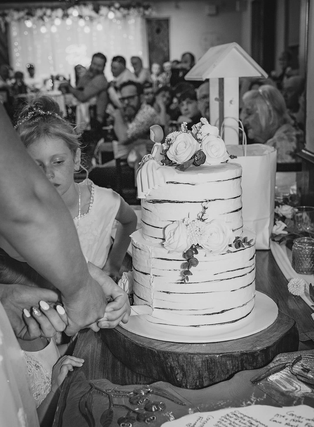 Black and white photo of the white cake being cut at the reception