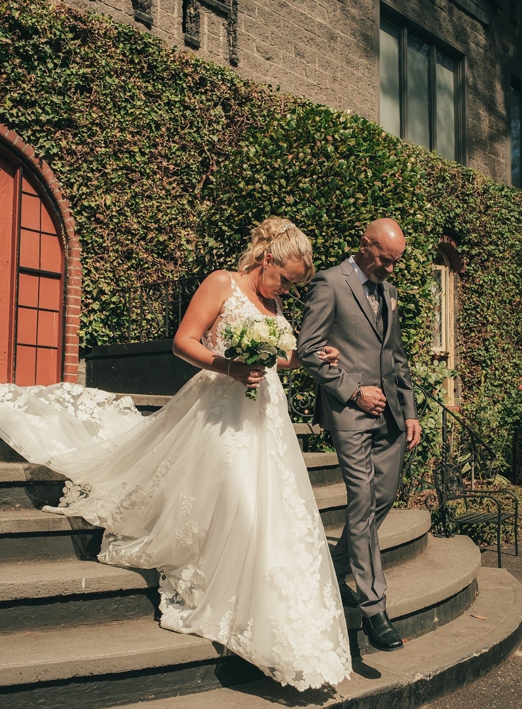 Jenna walking down the stone steps from the castle door with her train behind her