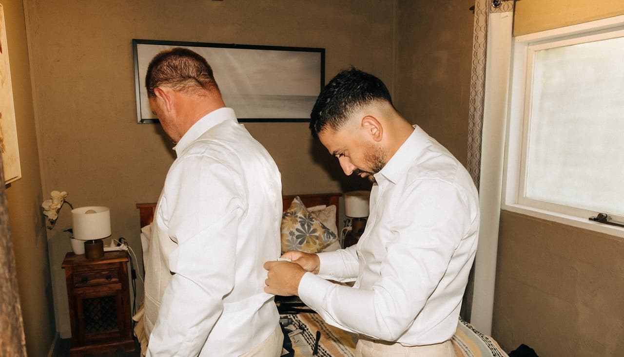 Two of the men buttoning their white shirts in the groom’s room