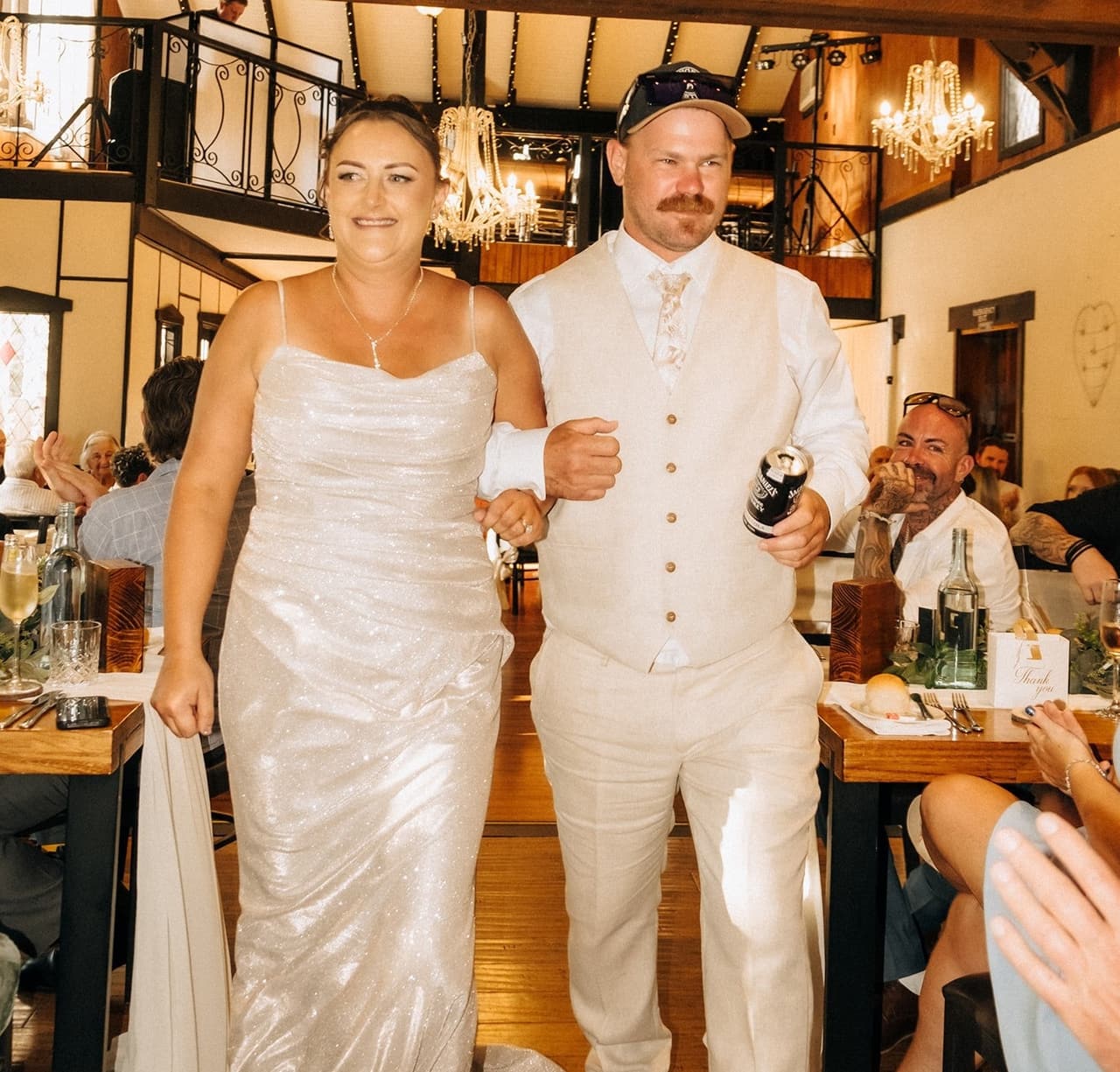 Jenna and Nick walking into the reception hall, laughing, guests at the long tables either side