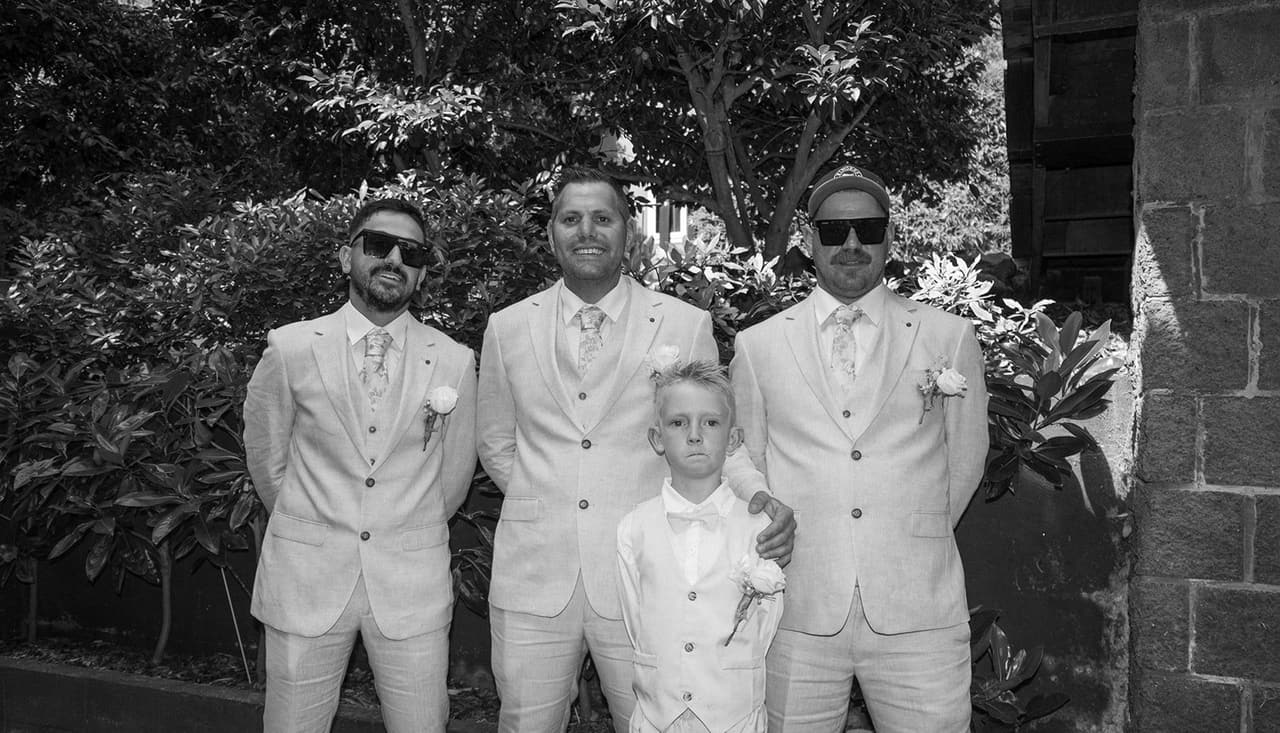 Black and white photo of Nick, his groomsmen and a page boy in front of the stone wall
