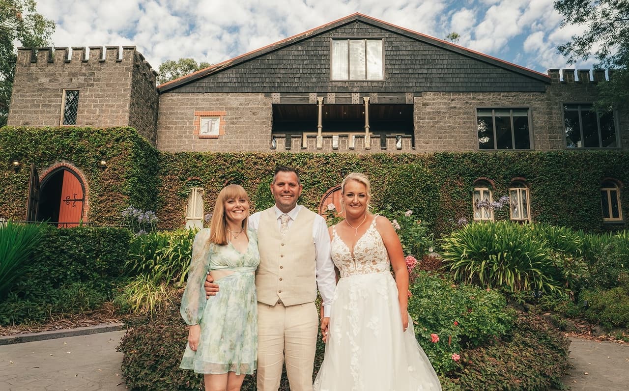 Jenna and Nick with a guest in a green dress in front of the castle and its tower