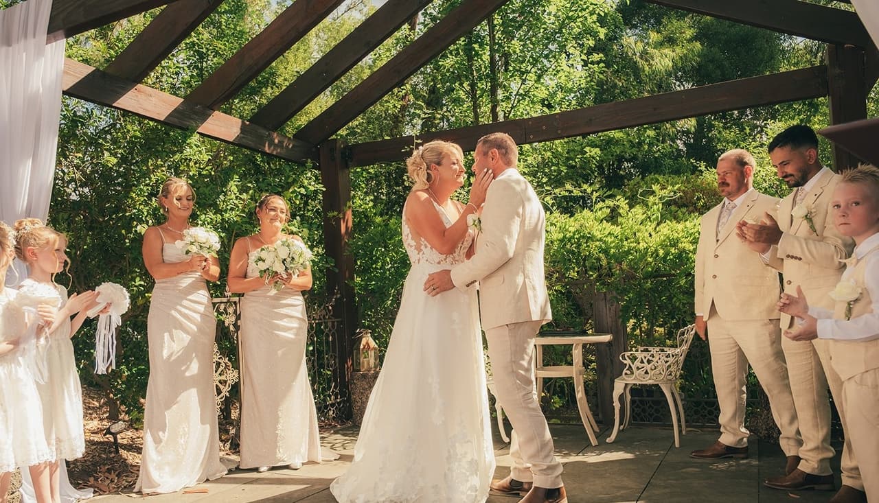 Jenna holding Nick’s face just before their kiss under the pergola as the bridal party claps