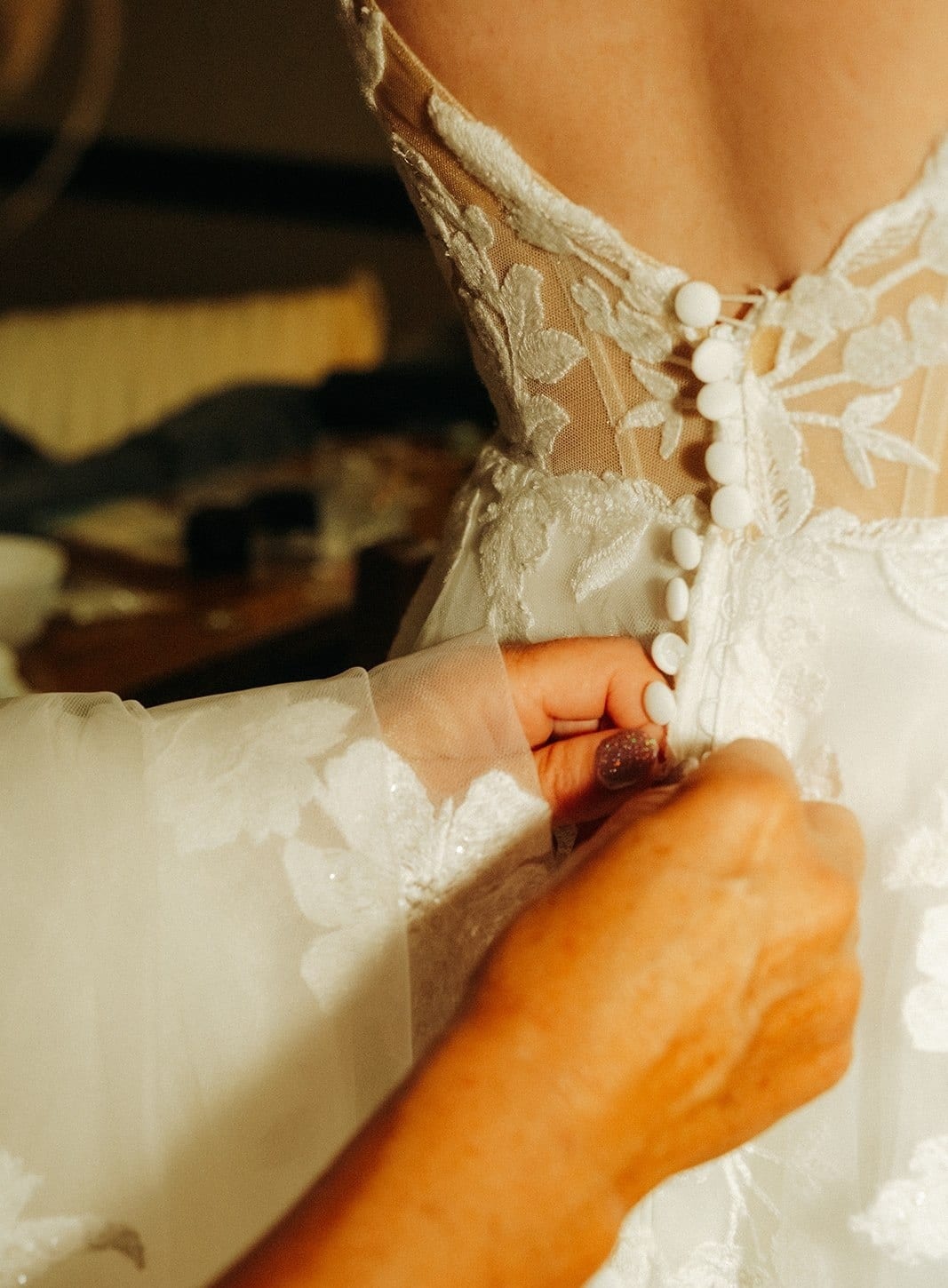 Close up of hands doing up the buttons on the back of Jenna’s lace gown