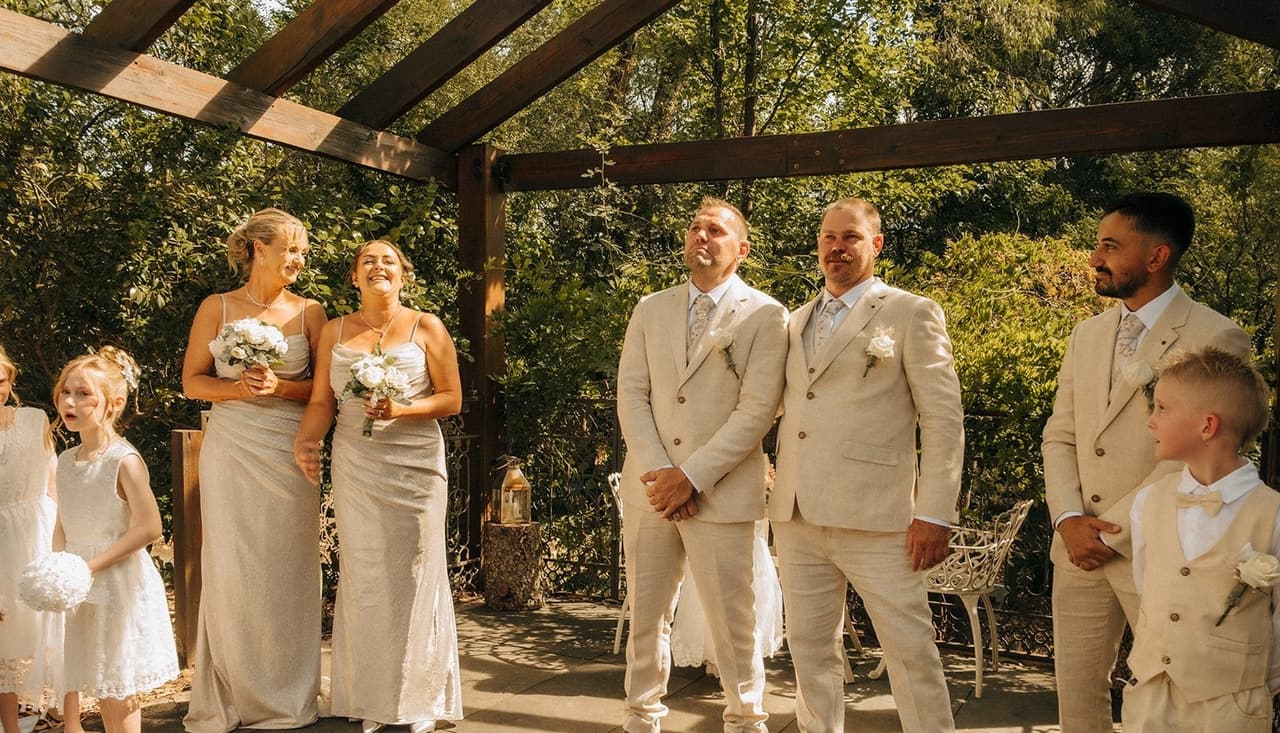 Nick, his groomsmen, a page boy and the bridesmaids waiting under the timber pergola