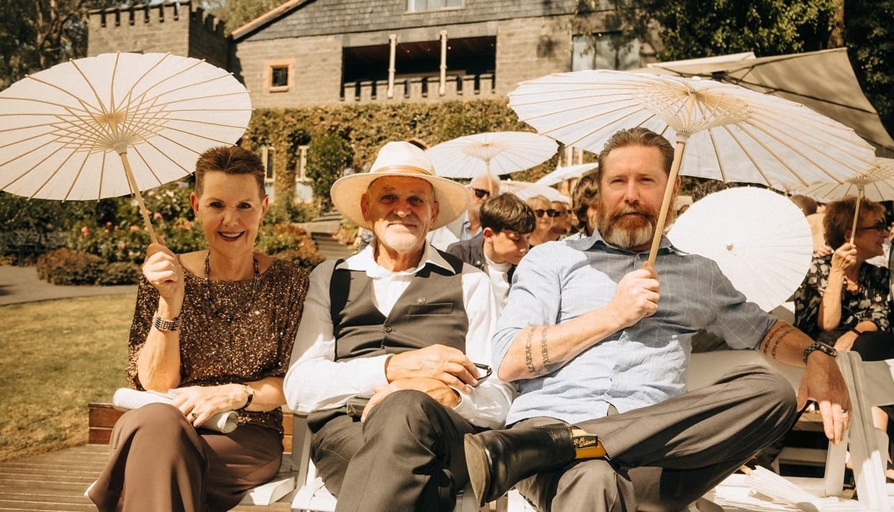 Guests laughing under white parasols on the ceremony deck, the castle behind them