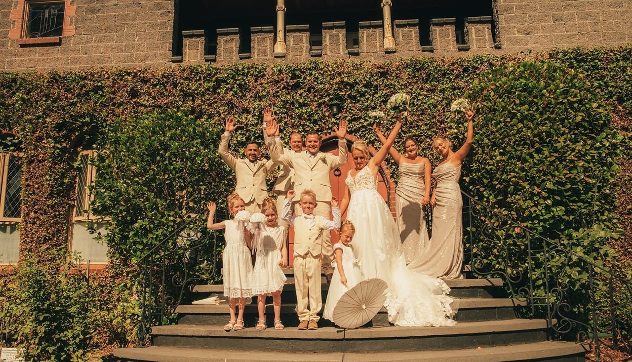 The bridal party throwing their arms and bouquets in the air on the castle steps