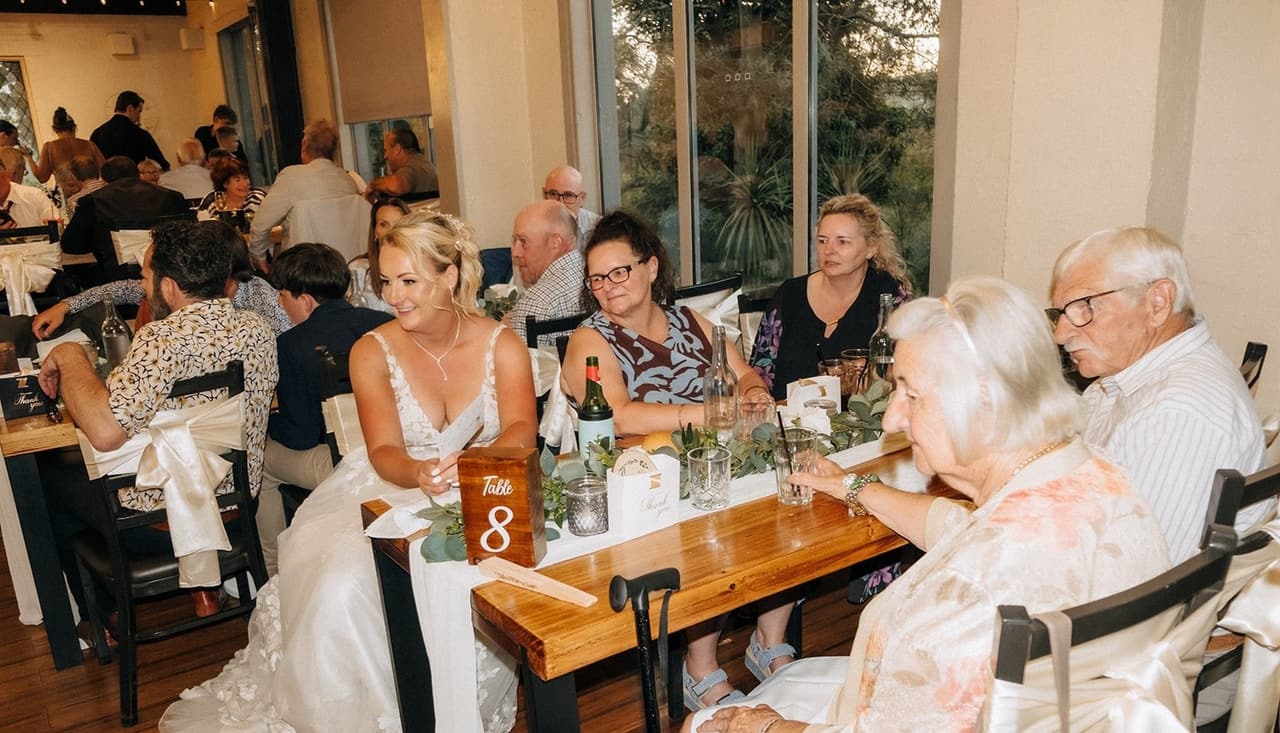 Jenna sitting with older guests at a long timber table during dinner