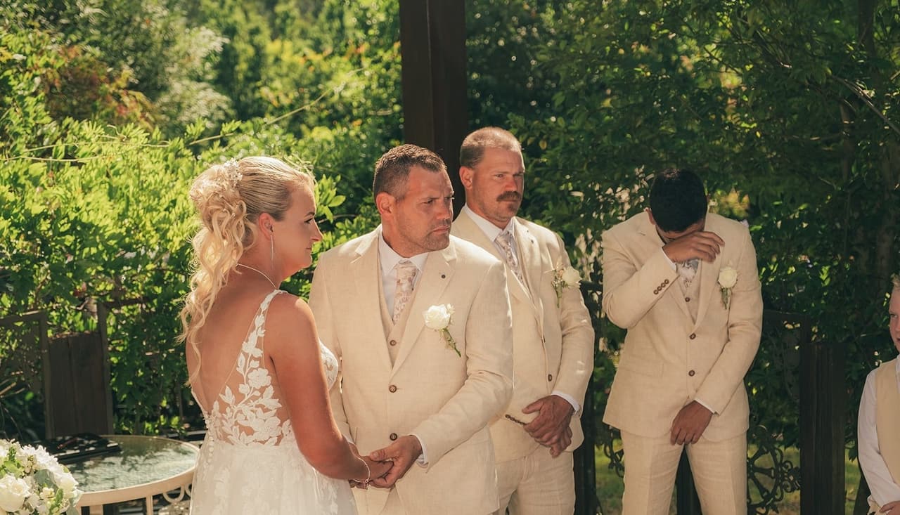 Jenna and Nick facing each other during the vows, a groomsman with his hand to his face beside them