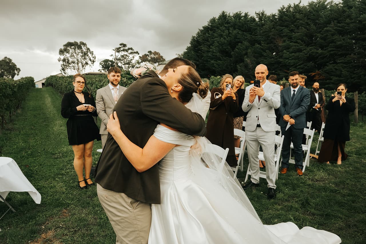 Max hugging Jessica as she reaches him at the end of the aisle, guests filming on their phones