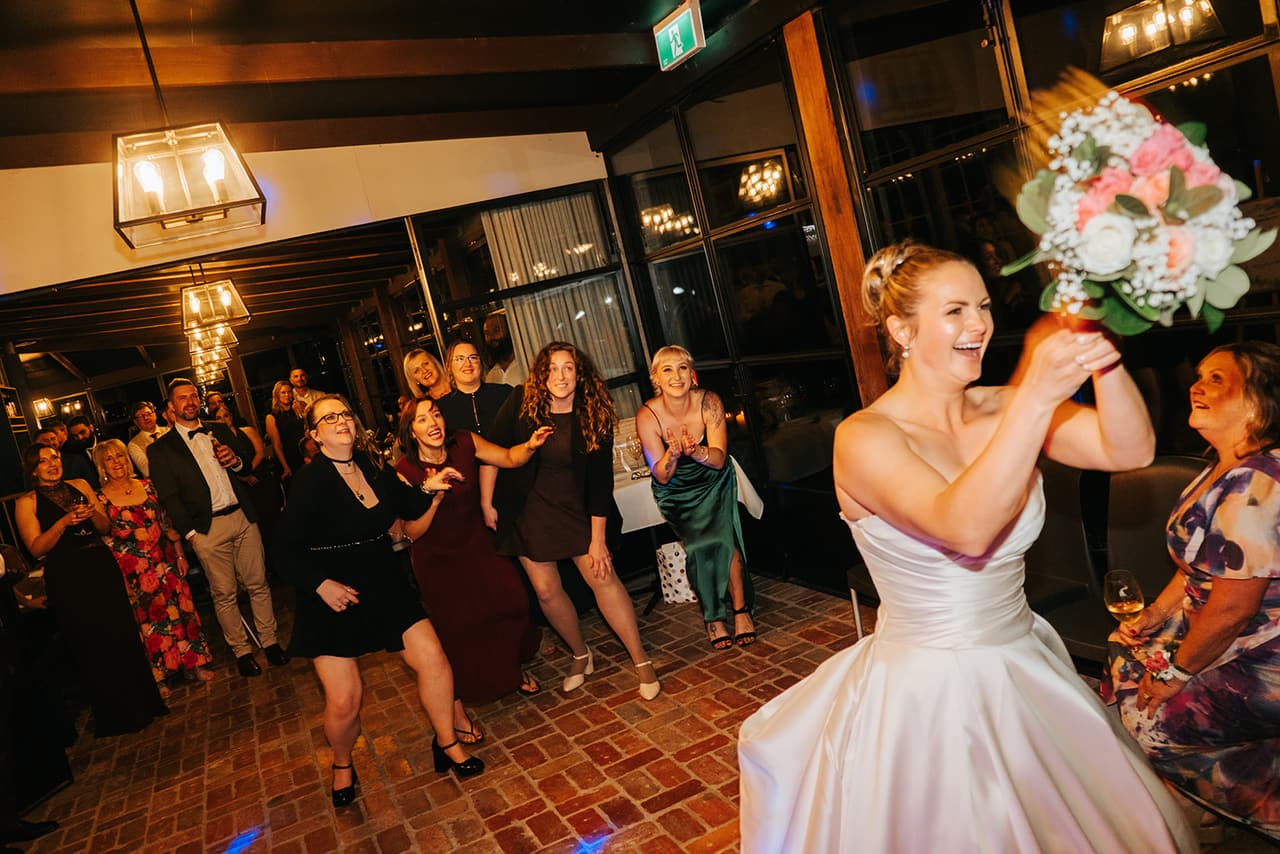 Jessica laughing as she throws her bouquet back over her head to the guests behind her