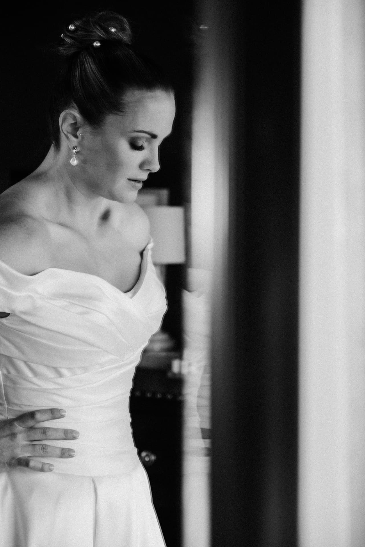 Black and white photo of Jessica in an off-shoulder gown looking down beside a doorway