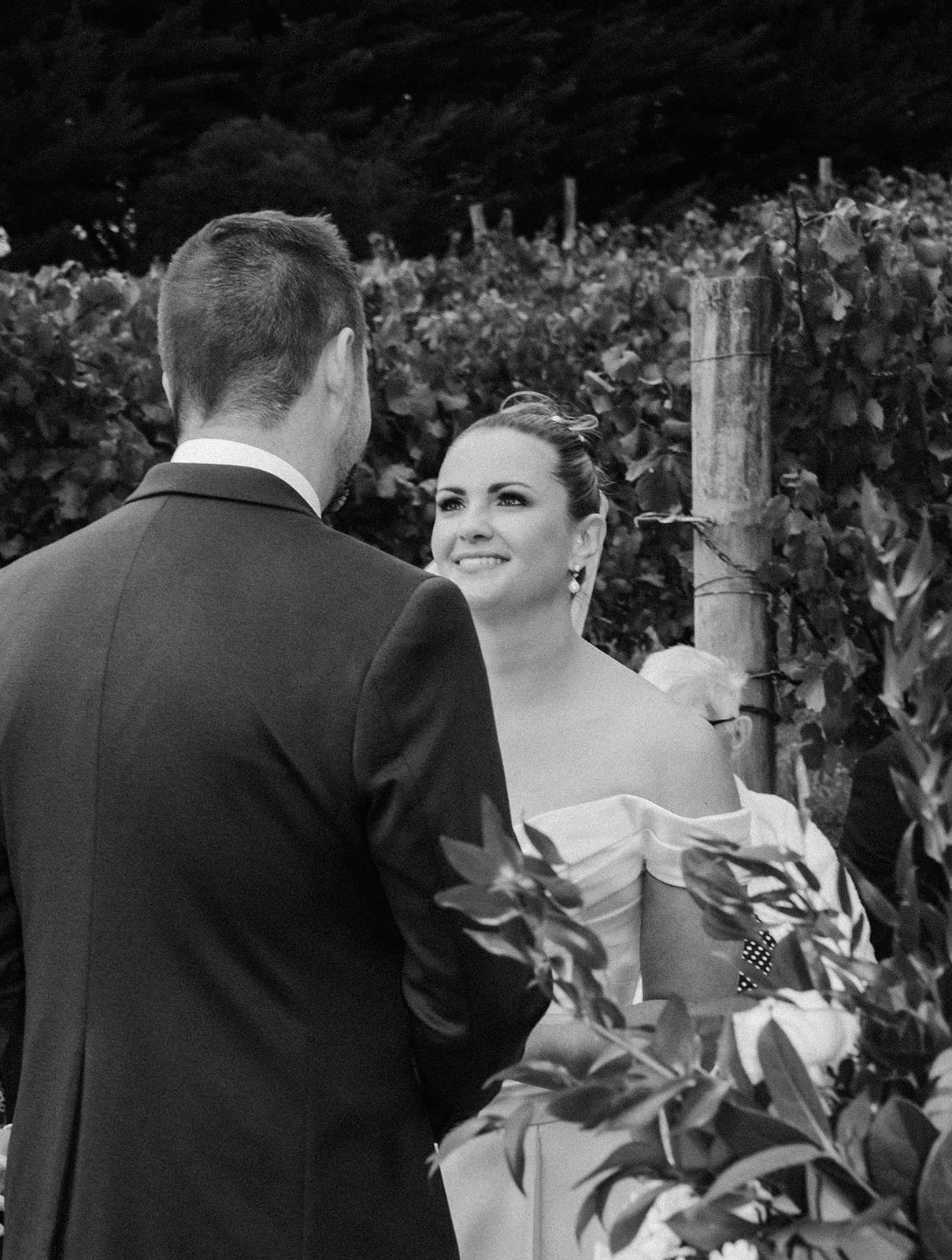 Black and white photo of Jessica smiling at Max over his shoulder during the vows